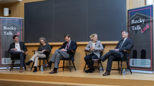 A photo of the panelists and hosts sitting on the stage in Hinman forum. 