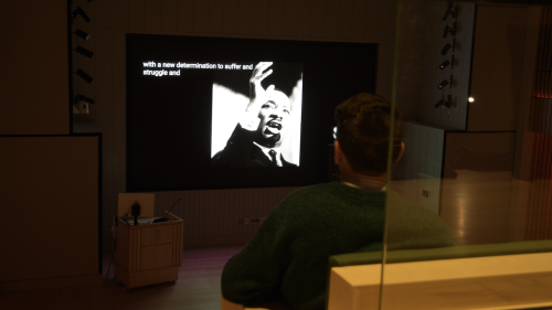 A student sits in a dark auditorium. A photo of Martin Luther King Jr. is on the screen.