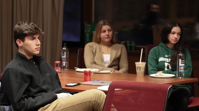 Three students sit and listen to a presentation.