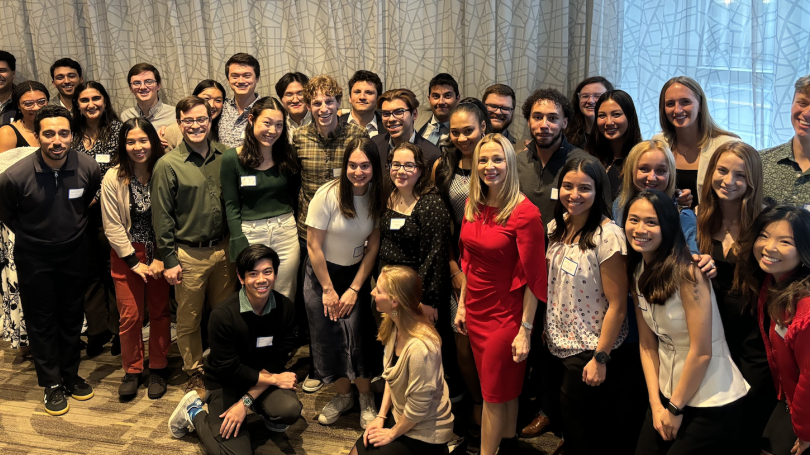 A group of Dartmouth alumni and students stand together in a hotel ballroom.