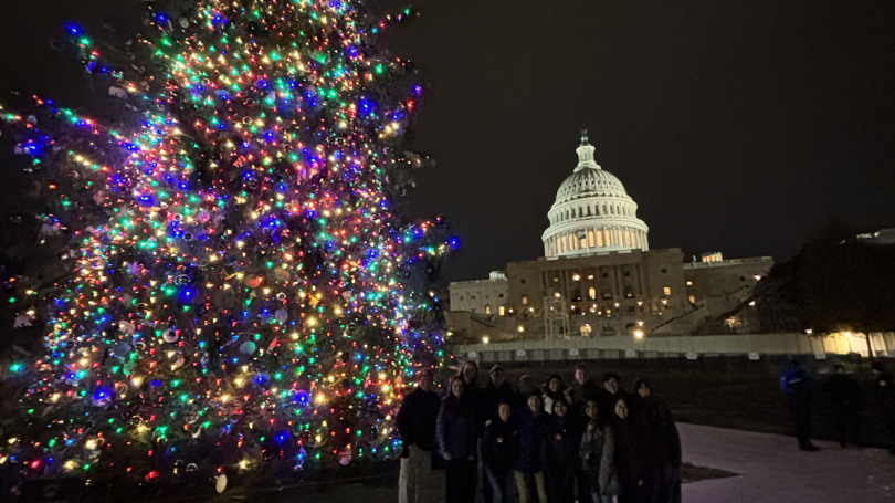 The RLF students stand outside at night. The US Capitol building is in the background and they are standing next to a large lit up Christmas tree.