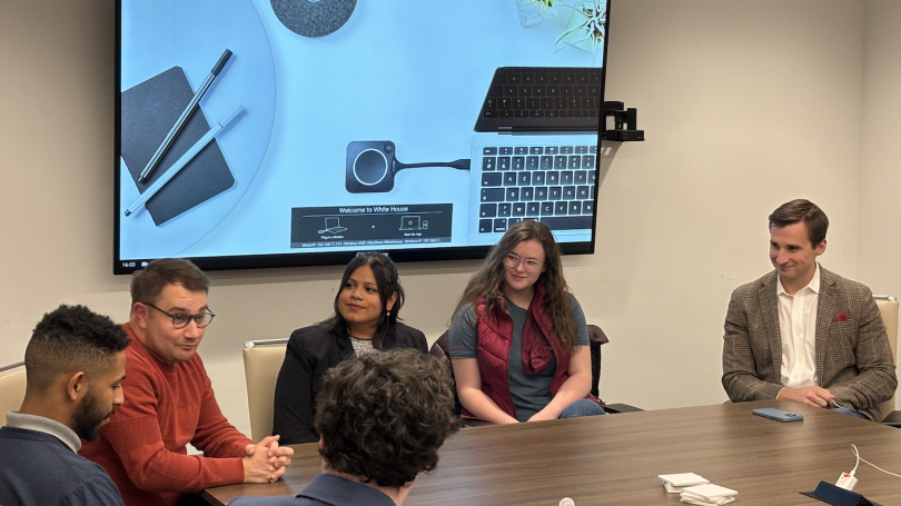 Several students and a speaker sit around a conference table talking.