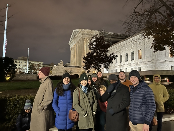 A group of students stand in front of the Supreme Court at night.