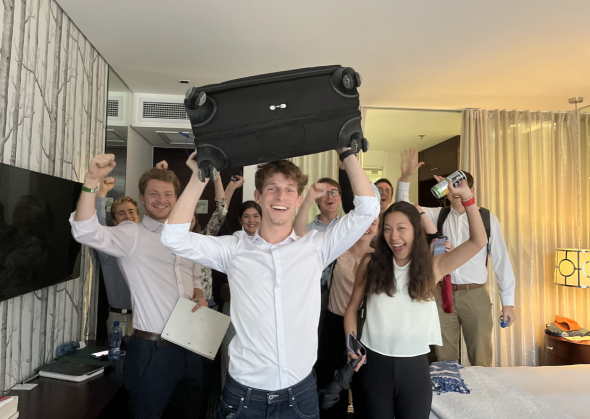 Josh raises his luggage above his head while his fellow students cheer
