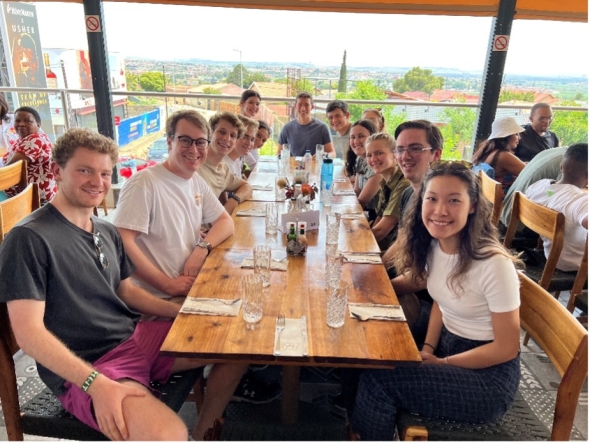 The students sit all together at a table at a restaurant.