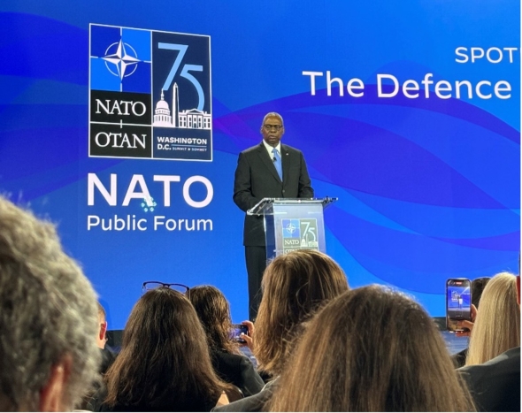 Lloyd Austin standing at a podium on the NATO summit stage.
