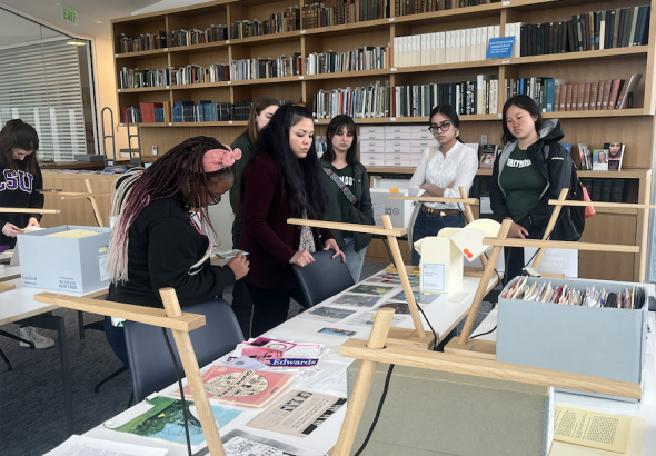 Students in the research center looking at a table with books and papers.